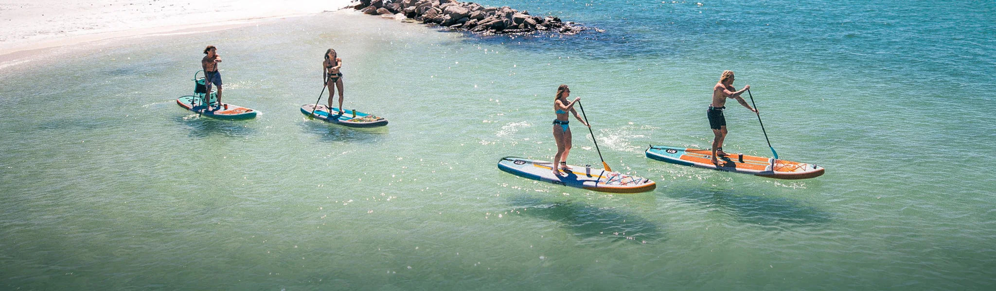 Four people paddleboarding on a clear blue sea with rocks in the background