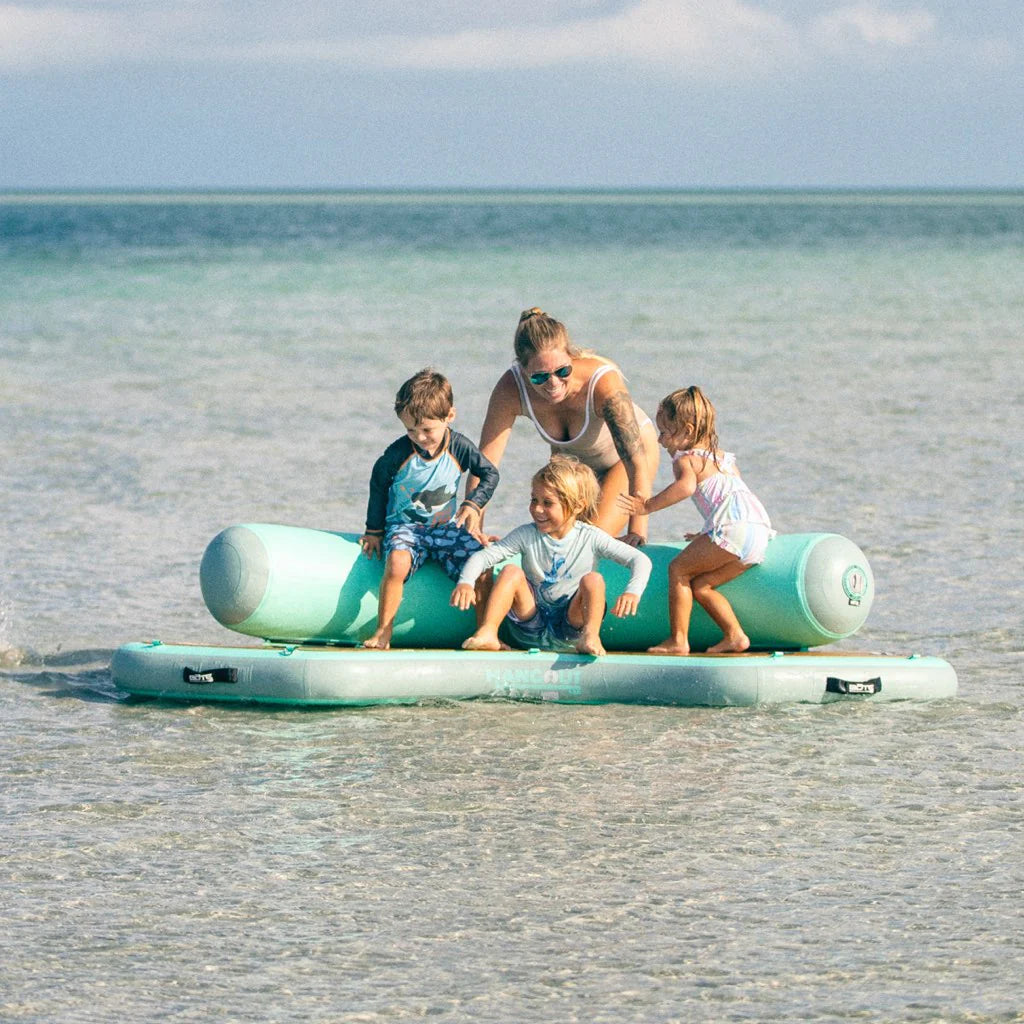 A family plays on the Inflatable Dock Hangout 120 Classic on the beach in the surf.