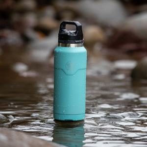 Front view of aqua MAGNEbottle with black lid standing in shallow water.