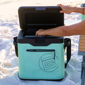 KULA Mule cooler open on sandy beach with hand reaching inside.