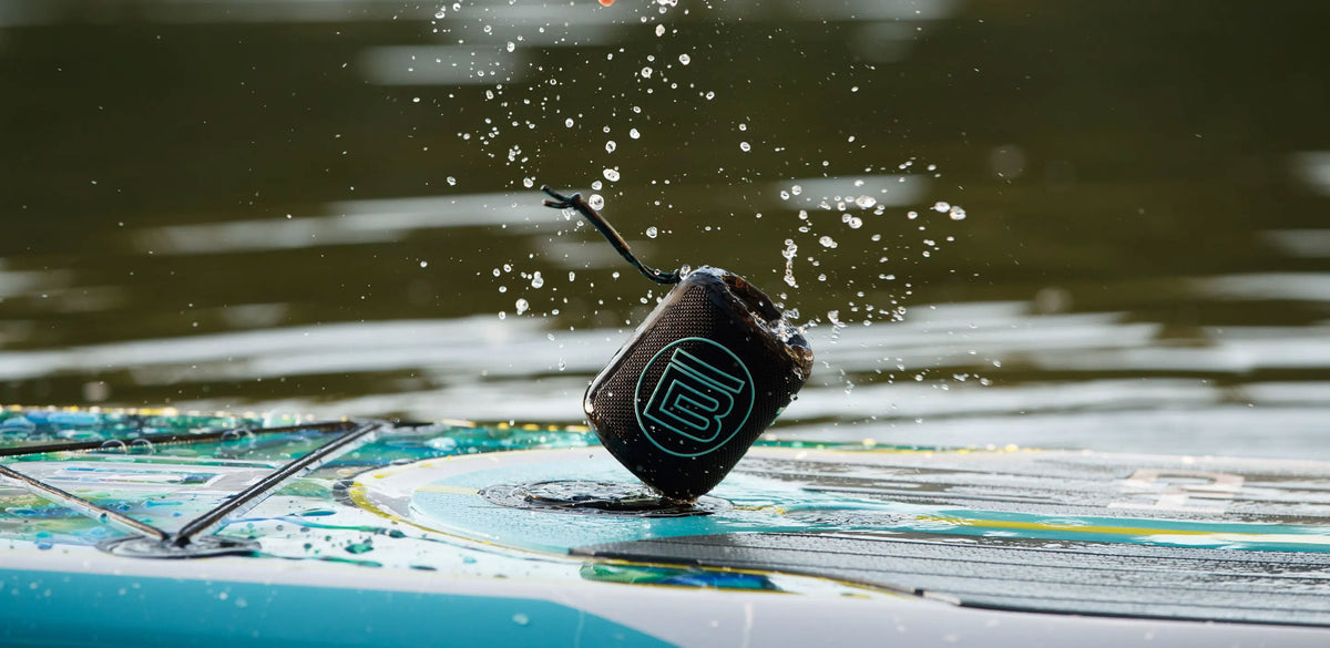 Angled view of black MAGNEPOD speaker attached to a wet paddle board.