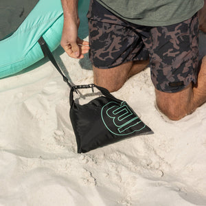Man burying a Hangout Anchor Kit sand bag in the beach to secure an inflatable shade shelter.